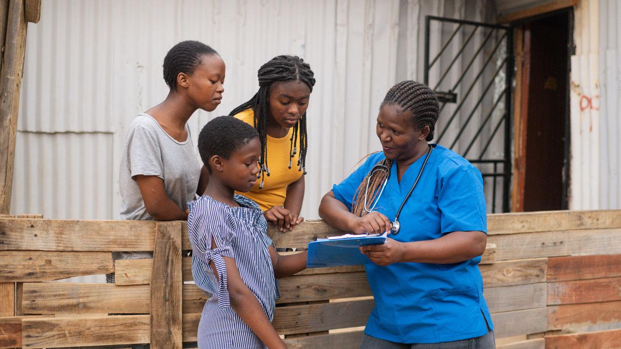 南非，三个女孩站在那里看着一名女医生拿着的药片